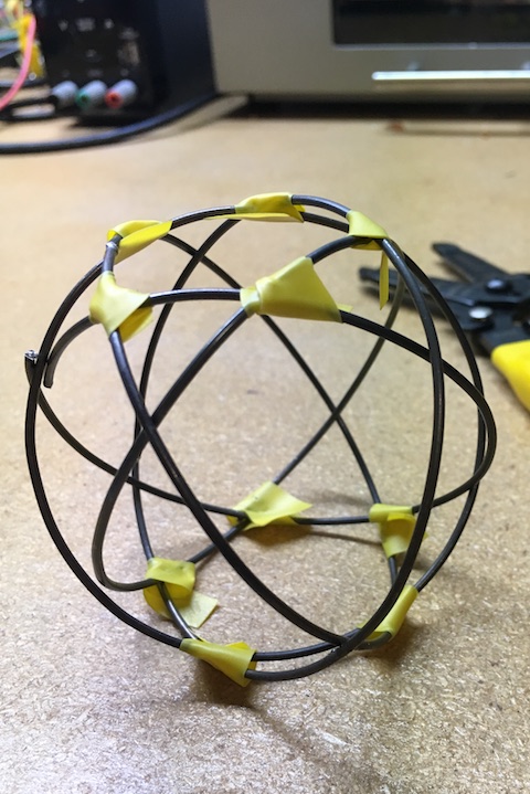 five rings of thick wire, tilted and rotated so they outline a sphere, with pentagonal holes at the top and bottom. small pieces of tape hold it together.